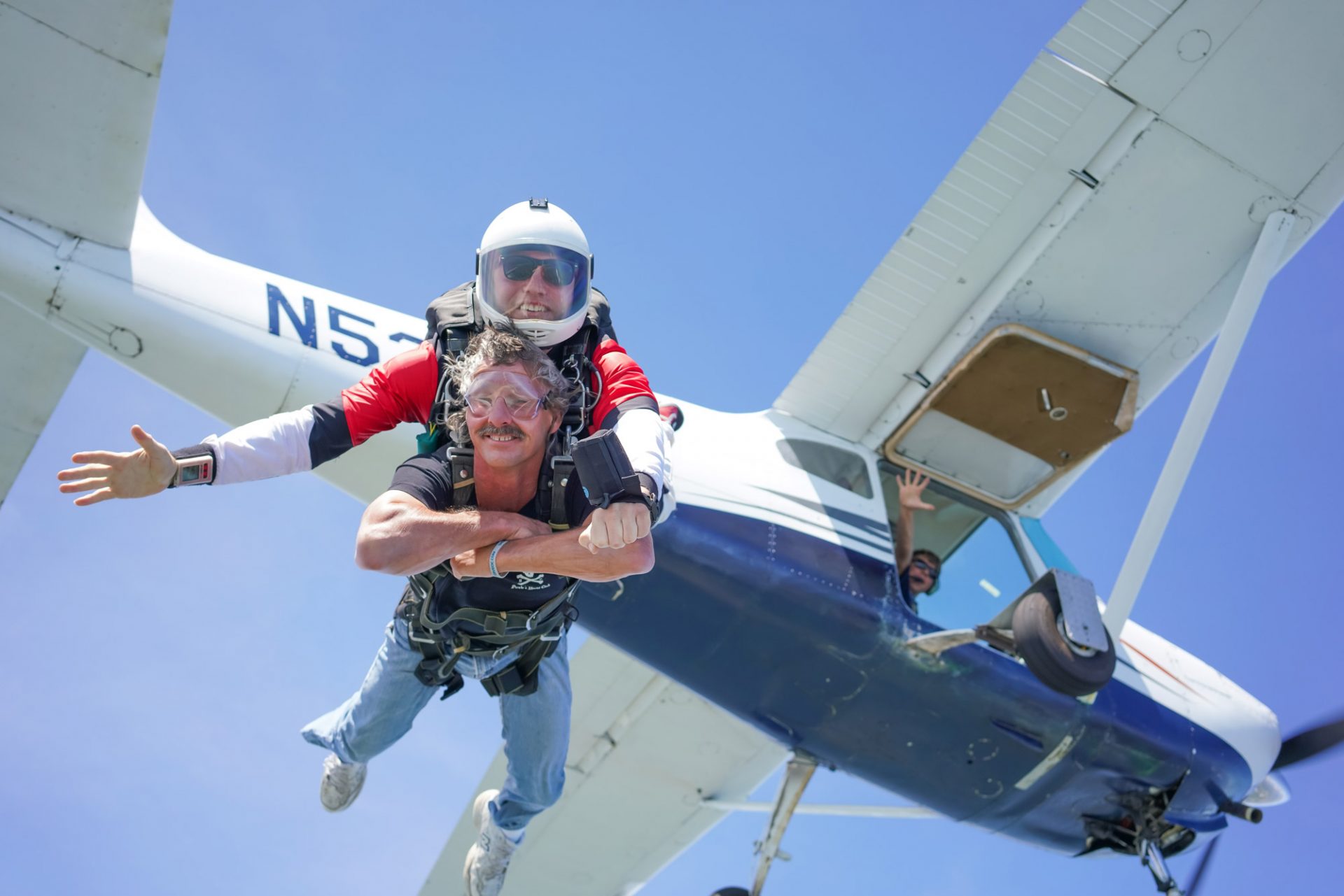 Male tandem skydiving student and instructor smiling for camera after exiting aircraft