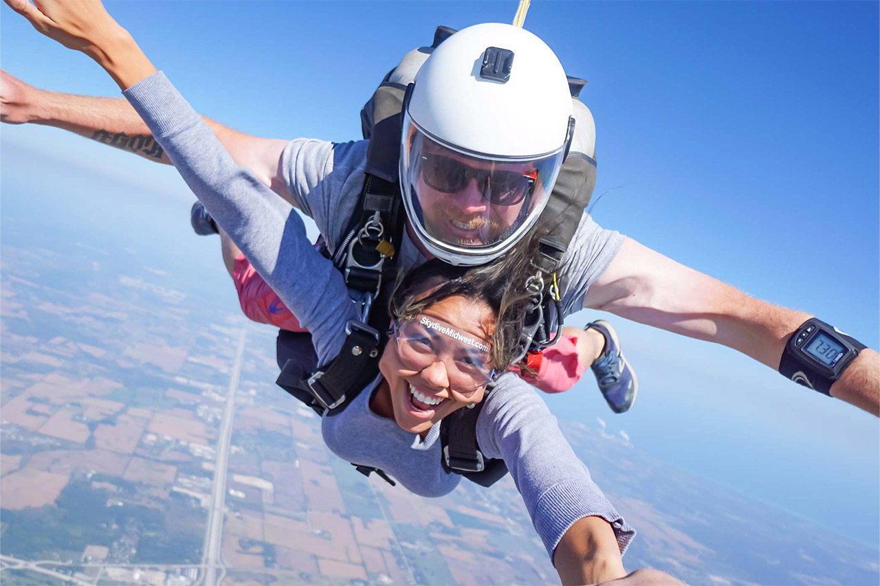 Female tandem skydiving student in freefall smiling at the camera