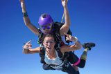 Female tandem skydiving student and instructor in freefall giving rock on sign with hands